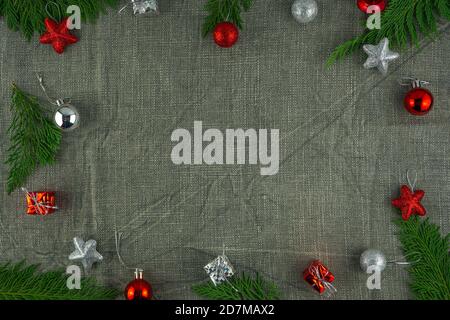 Christmas frame made of fir tree branches, red and silver Christmas toys and gift boxes on a gray burlap background. Flat lay. Top view with copy spac Stock Photo