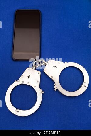 Handcuffs and Mobile Phone on the Blue Paper Background Stock Photo