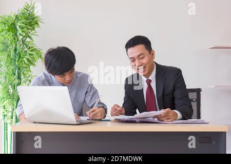 An Asian male supervisor teaches the newcomer to the office on his desk. Stock Photo