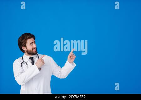 Horizontal banner of smiling young male doctor showing and presenting something with hand, isolated on blue background with copy space on the left Stock Photo