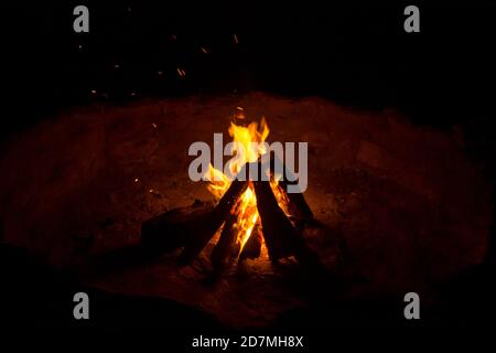 A wood fire burning in a wide outdoors fire pit outside during night Stock Photo