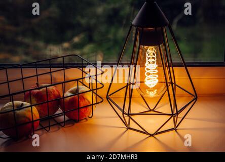 Modern black wire lamp with spiral light led bulb illuminated and wire basket next to it. Modern cozy interior with mood light. Stock Photo