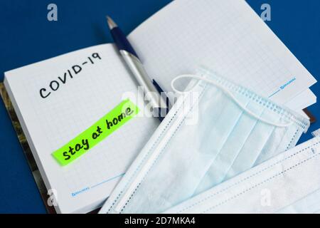 text coronavirus, stay at home, office there written on a Notepad by hand. the view from the top. mask and ballpoint pen with Notepad on a blue backgr Stock Photo