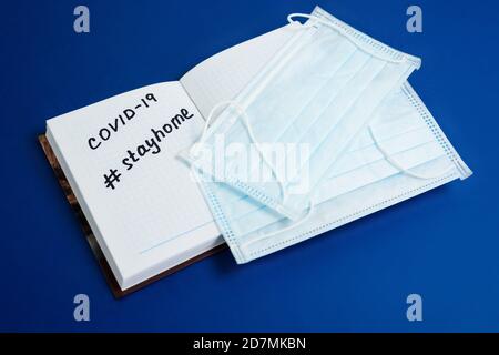 text coronavirus, stay at home, office there written on a Notepad by hand. the view from the top. mask and ballpoint pen with Notepad on a blue backgr Stock Photo