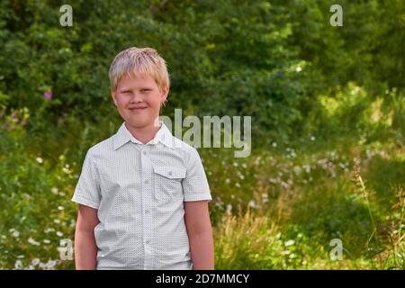 A smiling boy in a white shirt stands in a Park in summer. Portrait Stock Photo