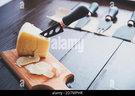 Composed cloesup detail view of aged cheddar cheese with cheese knife set, over vintage brown wooden backdrop Stock Photo