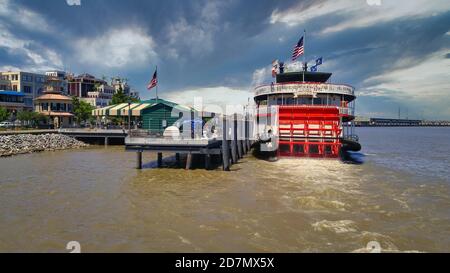 Port of New Orleans day light view showing The steamboat Natchez on Mississippi River with American flags,Skylines and clouds in the sky in background Stock Photo