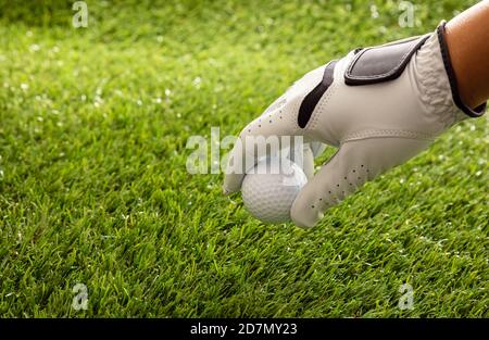 Hand in golf glove holding a golfball, green course lawn background, close up view. Golfing sport and club concept. Copy space, template Stock Photo