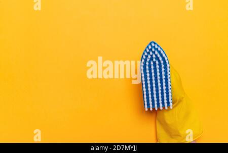 blue brush for washing clothes in a hand in rubber yellow gloves on a yellow background. place for text. Stock Photo