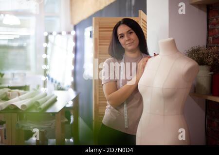 Pretty woman fashion designer standing and holding mannequin in workshop Stock Photo