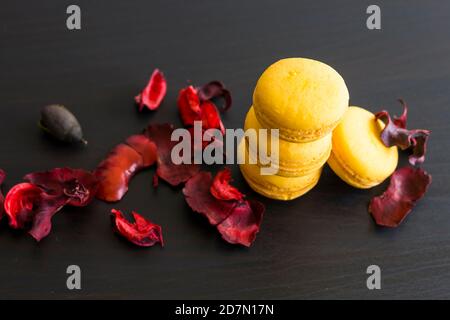 Close-up of breakfast morning with yellow macaroons lemon taste. close-up of french dessert on the black background and flowers around in a simple vin Stock Photo
