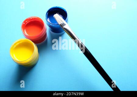 Color oil paint in plastic containers on blue with a black paintbrush. Stock Photo