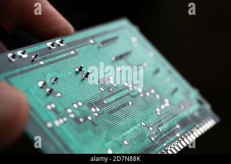 Fingers hold a green electronic circuit board with many electrical components against a black background Stock Photo