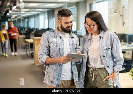 Two happy young intercultural office managers discussing working points or ideas Stock Photo