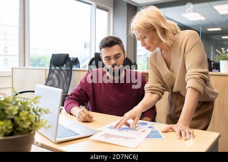 Blond mature businesswoman discussing diagrams and charts with male colleague Stock Photo