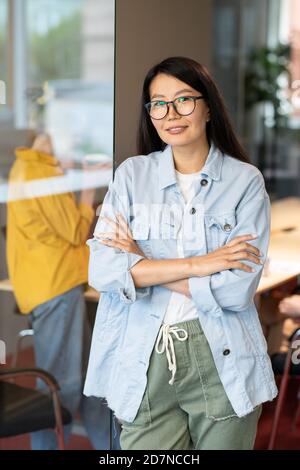 Happy young Asian businesswoman crossing her arms by chest against colleague Stock Photo