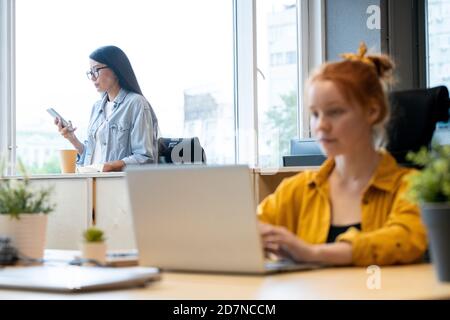 Young serious Asian businesswoman in casualwear looking at smartphone screen Stock Photo