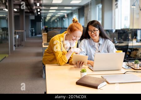 Two young laughing intercultural businesswomen looking at tablet screen Stock Photo