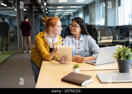 Two young intercultural female managers looking at one another with smiles Stock Photo