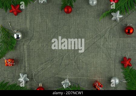 Christmas frame made of fir tree branches, red and silver Christmas toys and gift boxes on a gray burlap background. Flat lay. Top view with copy spac Stock Photo