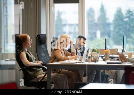 Happy mature businesswoman making notes by desk between two young colleagues Stock Photo