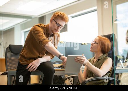 Young confident managers in casualwear discussing information on tablet screen Stock Photo