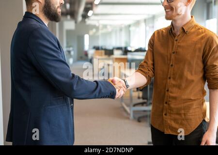 Handshake of two young male colleagues in casualwear standing in the aisle Stock Photo