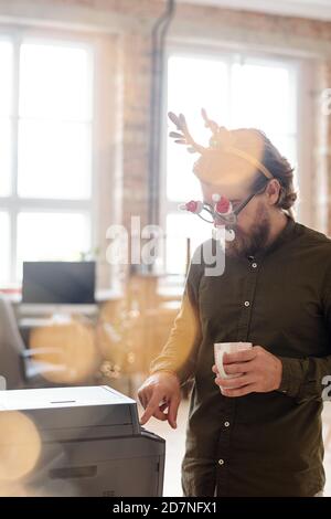 Young businessman in xmas eyeglasses pressing start button to copy document Stock Photo