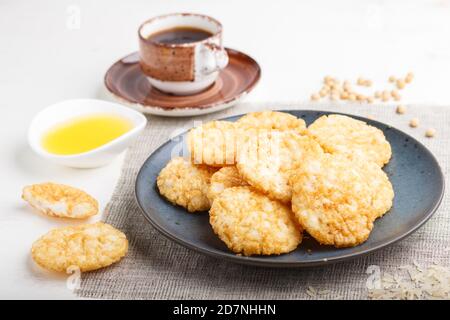 Traditional japanese rice chips cookies with honey and soy sauce on a blue ceramic plate and a cup of coffee on a white wooden background. side view, Stock Photo