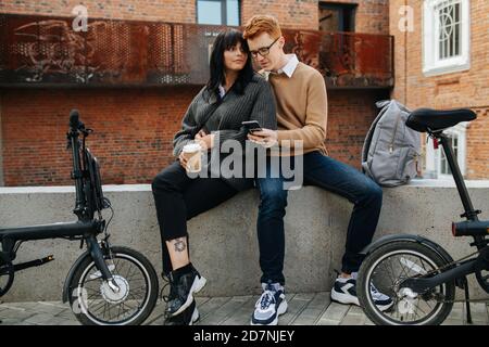 Man and woman in love sitting on a concrete border close to each other. Stock Photo