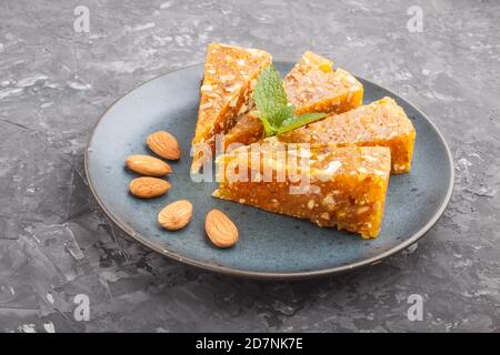Traditional turkish candy cezerye made from caramelised melon, roasted walnuts, hazelnuts, pistachios in blue ceramic plate on a black concrete backgr Stock Photo