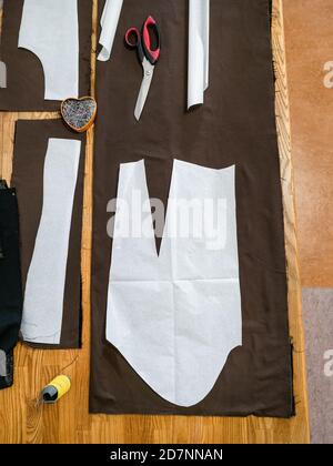top view of sartorial tools and patterns layouts of dress on brown fabric on wooden table at home Stock Photo