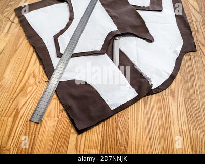 steel rule lays on a layout of sewing patterns of dress on brown fabric on wooden table at home Stock Photo