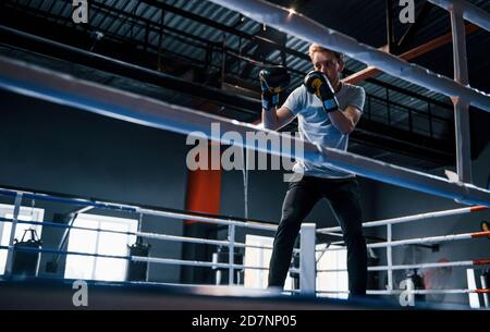 Young man in white shirt and protective gloves doing exercises in boxing ring Stock Photo