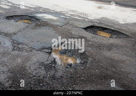 Potholes on a paved road. The road is in very poor condition. There is dirty water in the potholes. Stock Photo