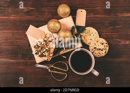 Christmas flat lay composition with coffee cup, cookies, gift boxes and golden baubles on dark background. Stock Photo