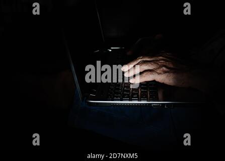 Side view of crop wrinkled hand of unrecognizable senior businessman working with electronic information on laptop in dark room. Stock Photo
