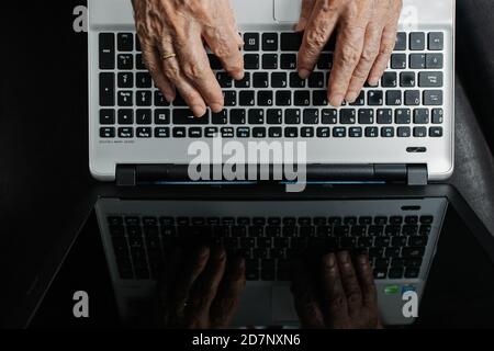 Top view of crop anonymous aged remote worker typing on laptop keyboard while sitting at table in workplace. Stock Photo