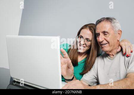 Positive mature man and woman hugging and communicating with friends via video chat on laptop. Stock Photo