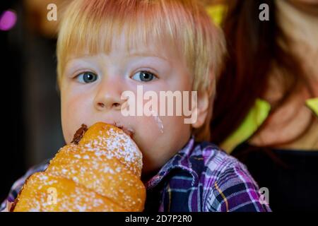 Beautiful kid eating croissant bun chocolate the table in paper bag closeup hand little boy having breakfast in cafe Stock Photo