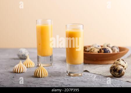 Sweet egg liqueur in glass with quail eggs and meringues on a gray and orange background. Side view, close up. Stock Photo