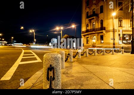 Granite posts with chains. Abstract night city blurred lights of moving cars for decoration design. Yellow background. Abstract background. The dark blue sky Stock Photo