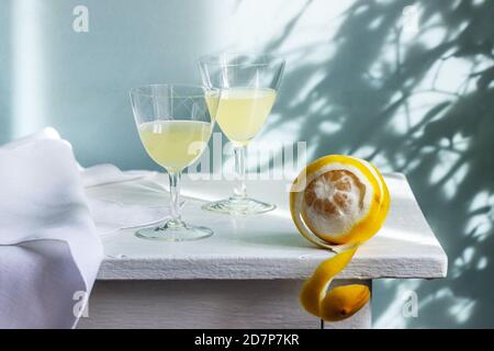 Italian liqueur limoncello in crystal glasses and ripe lemons on a wooden table. Stock Photo