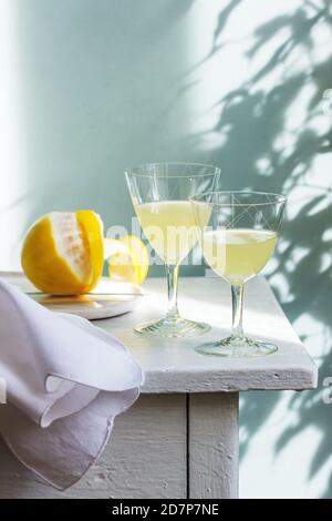 Italian liqueur limoncello in crystal glasses and ripe lemons on a wooden table. Stock Photo