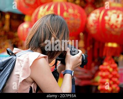 Female Chinese photographer takes a photo of colourful good-luck souvenirs and traditional red-and-gold paper lanterns at Chinese New Year. Stock Photo