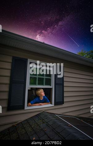 Young boy views moon and star galaxy,  from bedroom window. Stock Photo