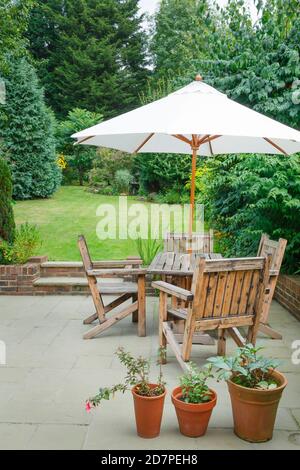 Suburban UK back garden in summer with patio, wooden garden furniture and a parasol or sun umbrella Stock Photo