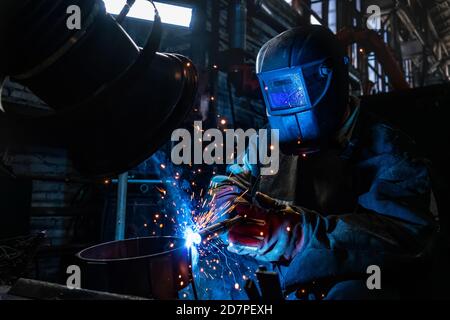 Side view of welder in protective helmet welding metal detail with sparks at factory Stock Photo