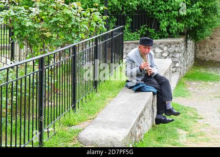 Elderly azeri man playing on balaban ,local wind musical instrument ,for Great Silk Road tourists at entrance to ancient christian Albanian church.  Stock Photo