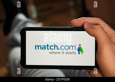 Match com logo on the screen of mobile phone in mans hand. Application for dating and acquaintance. Man is laying on the sofa and looking for partner Stock Photo